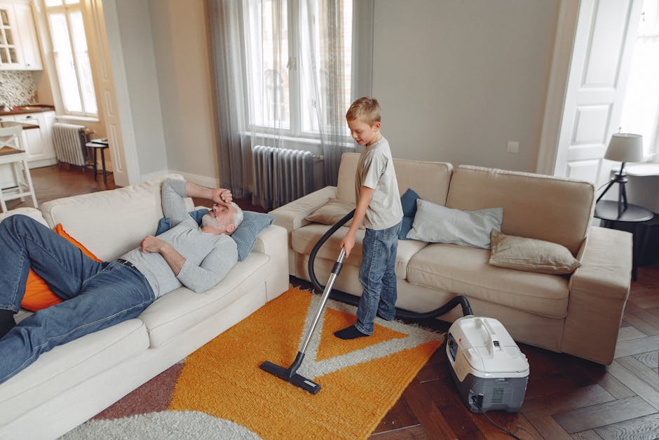 A person wearing a full protective suit, gloves, face mask, and shoe covers performs deep carpet cleaning in a bright, minimalist living room. They are using a professional cleaning machine with a lon